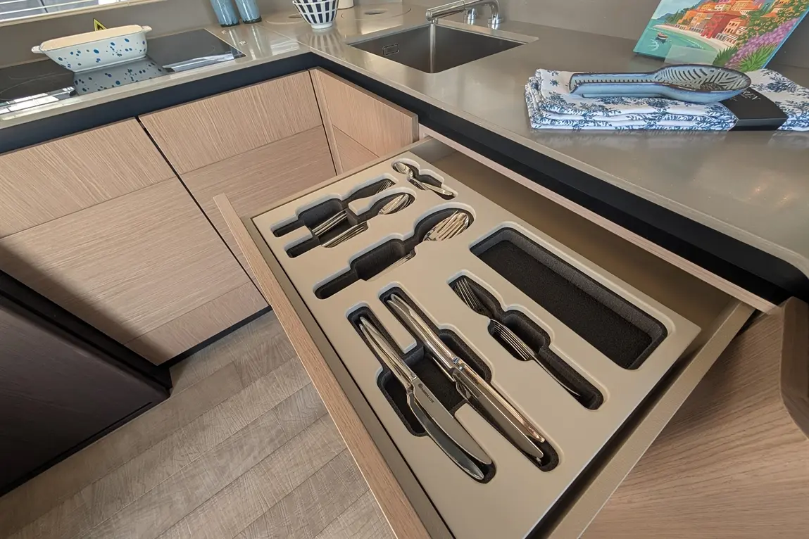 Kitchen drawer with neatly arranged cutlery and utensils, including knives and forks, against a modern cabinetry backdrop.